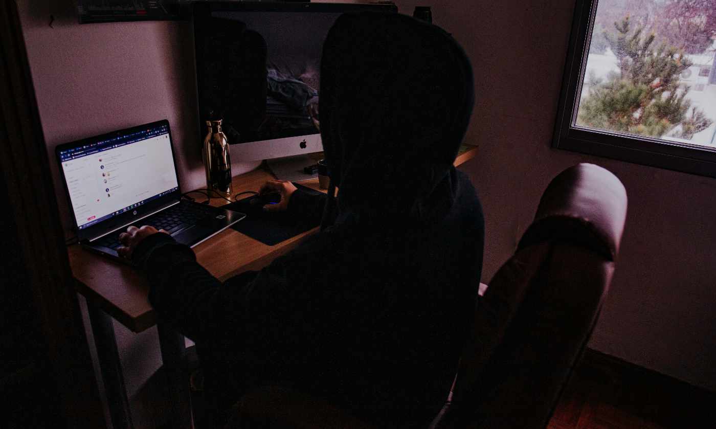 Person sitting in front of a computer with face obscured and dimly lit.